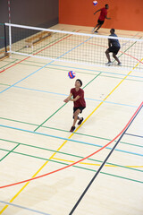 Diverse male players with Asian teen preparing forearm pass, playing on hardwood gym court near net