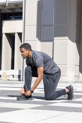 African American man kneeling and tying running shoe on patterned plaza while wearing smartwatch © wavebreak3