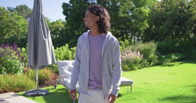 African American man in his 20s noticing camera moving in, fixing hoodie, smiling near umbrella