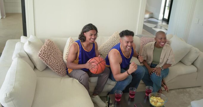 African American friends in jerseys cheering after big basket on TV, holding basketball with chips