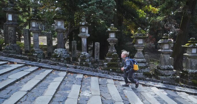 Child walking up stone steps near line of mossy, ancient, stone ishidoros - tracking shot