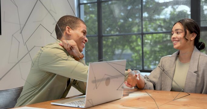 Shaking hands man in green shirt and woman in grey blazer in office, silver laptop