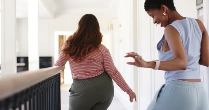 African American women friends walking hallway one leading other playfully following using banister