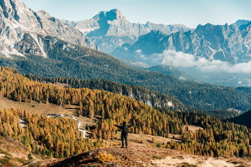 A man backpack stands overlooking autumn larch forest and Dolomites mountain in Italy © Mumemories