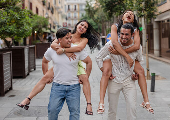 Naklejka premium Cheerful couples giving piggyback rides on a city street