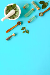 Homemade organic cosmetics products - tea tree essential oil and sea salt in mortar and pestle with green leaves on blue background, top view