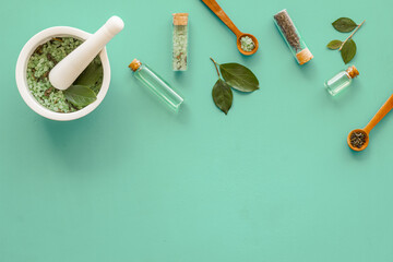 Homemade organic cosmetics products - tea tree essential oil and sea salt in mortar and pestle with green leaves on green background, top view.