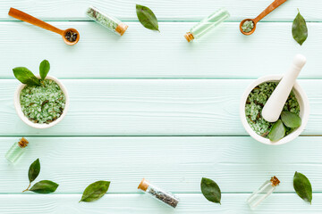 Frame of tea tree essential oil and sea salt near green leaves top view. Organic cosmetics products.