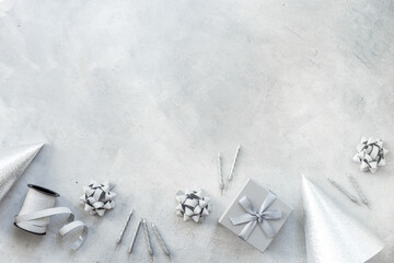 Holiday festive party flat lay with silver carnaval caps and cake candles, top view. Gift box and streamers on gray stone background