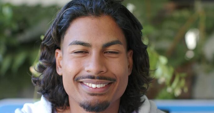 African American male wearing hoodie smiling widening grin after camera cue on blue bench
