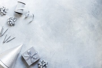 Holiday festive party flat lay with silver carnaval caps and cake candles, top view. Gift box and streamers on gray stone background