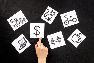 Hand is choosing Dollar card from many paper cards with hand drawing of different life activities. Life balance concept.