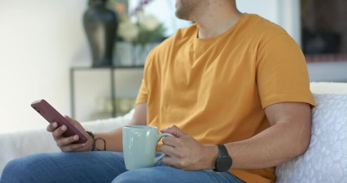 Man is holding smartphone and light-blue mug on sofa while phone is vibrating, turning right