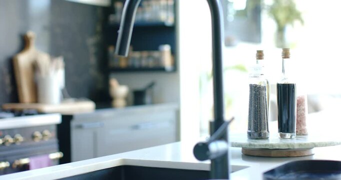 Camera is panning left and is racking focus on island, revealing black faucet, tray, spice rack