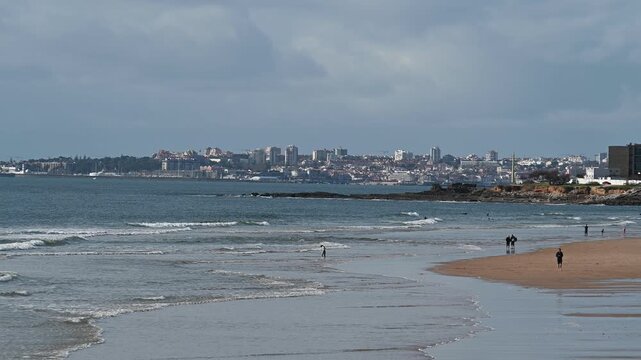 People walking along shallow ocean water near Cascais