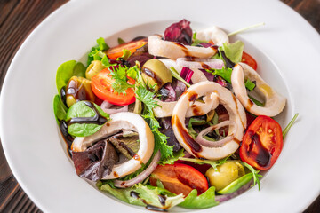 Mediterranean squid salad with arugula olives and tomatoes on white ceramic plate