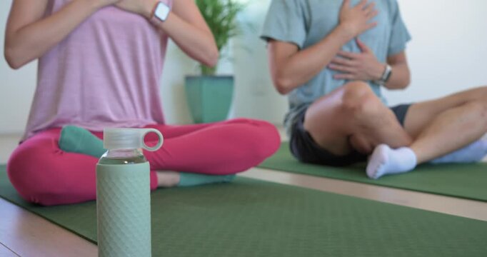 Couple doing mindful breathing on yoga mats at home as camera refocusing with mint bottle front