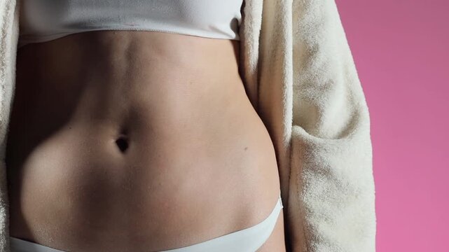 HD slow motion closeup of woman shaking belly fat with hand showing body fat movement for skincare and health care concept on pink background