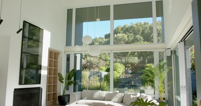 Camera is beginning tilt back, revealing tall glazing, pendant lights, sofa and plants to show room