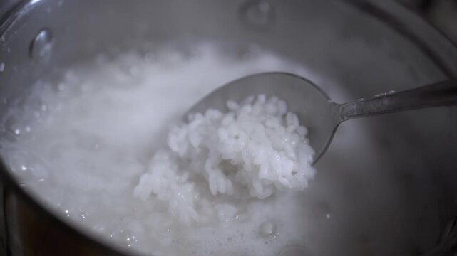 A close-up shot of a spoonful of rice being lifted from a pot of simmering rice porridge. This shot emphasizes the texture of the rice and the cooking process.