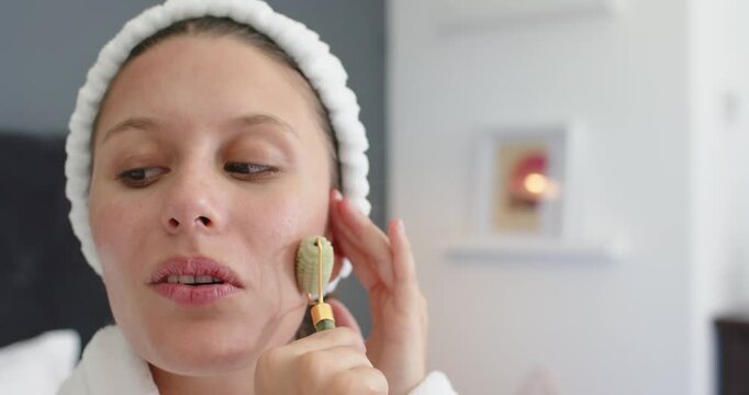 African American woman starting skincare using green roller, gliding up right jawline