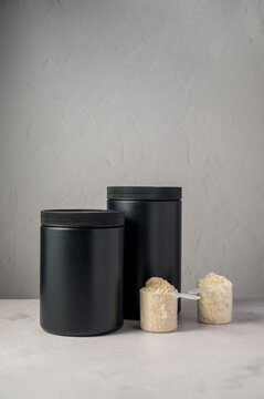 Protein powder in scoops with black protein tubes, jars in background. Body building, muscle growth and food supplement concept