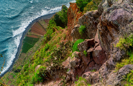 Vertical drop view from a rugged red sea cliff to coastal terraces.