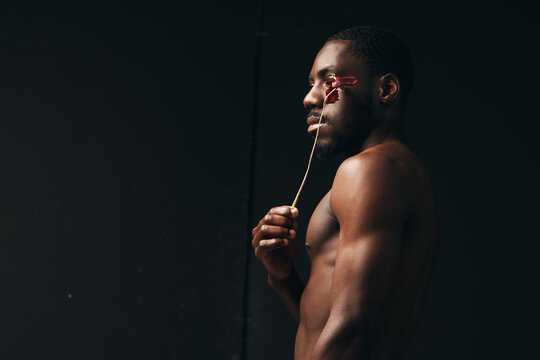 Creative visual designer style portrait of dark skinned African American man holding dried flower near face with bare torso on black background in artistic concept.