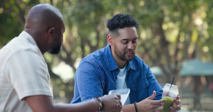 Diverse men sitting park bench eating from plastic tub and checking green drink as passerby passing