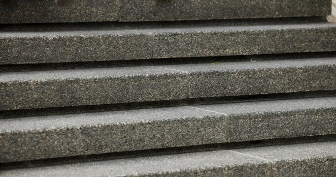 Pedestrians are coming from right and ascending textured concrete steps to reach building entrance