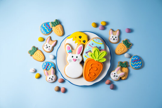 Easter holiday background with easter cookies in a plate: bunny, chick, carrot and egg on blue background, with mini chocolate egg candies