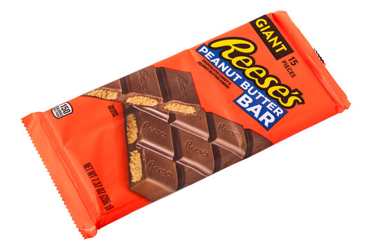 A giant Reese's peanut butter bar is seen on a store shelf. The bright orange packaging shows clear images of the candy and includes the brand name and size details.