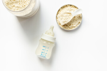 Baby milk bottle and powdered infant formula in the jar and scoop on white background. Top view.