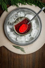 A jar and a spoon of red salmon caviar on silver plate with ice. Seafood with omega-3. Top view