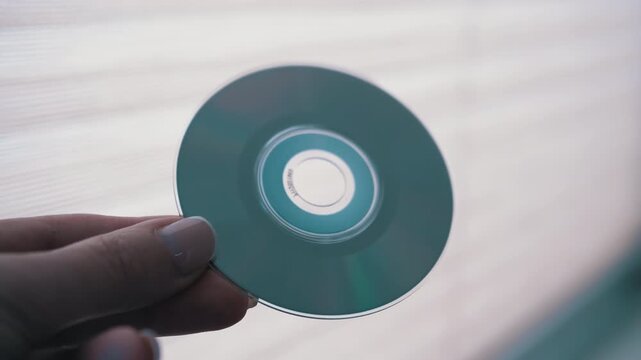 A hand holds a CD against a bright background, revealing its translucent surface and data grooves. Ideal for technology and data storage themes.