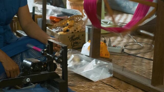 Silk spinning process at silk factory, Chiang Mai, Thailand. Woman spun red dyed silk threads on traditional wooden reel. Artisanal craftsmanship of textile production, sericulture process