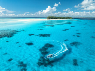 Aerial view of floating boat in transparent azure water on sunny summer day. Mnemba island, Zanzibar. Top view of yacht, sandbank in low tide, clear blue sea, sand, sky with clouds. Motorboat in ocean © den-belitsky