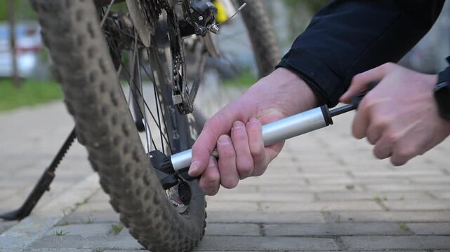 Men's hands blow out a bicycle wheel outdoors on the street at a bus stop