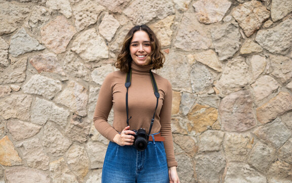 Woman with camera smiling against stone wall background