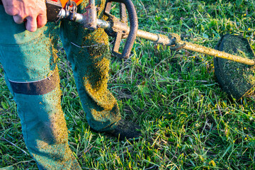 Worker Cutting Grass with Brush Cutter at Sunset