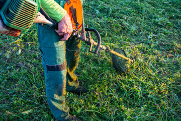 Obraz premium Worker Cutting Grass with Brush Cutter at Sunset