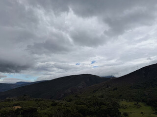 Spectacular mountain range beneath a dark, overcast sky with thick clouds and a lush green valley.