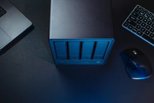 NAS Server Tower With Blue Lighting On Desk Beside Laptop Keyboard And Mouse In Modern Tech Workspace