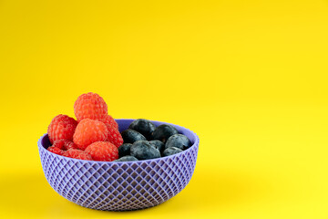 ibrant composition of forest fruits in a geometric bowl, featuring high contrast yellow and purple colors with copy space