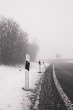 Roadside delineator posts along a snowy highway in thick winter fog.