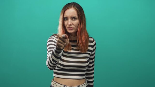 Woman points finger directly at camera in studio, striped crop top visible, stern accusing expression and confronting pose that addresses viewer; accusation.