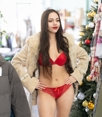 Young woman selects and tries on lace lingerie and fur coat in fashion boutique decorated for New...