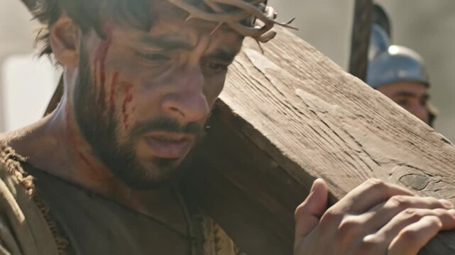 Biblical representation of Jesus christ carrying wooden cross with crown of thorns during crucifixion reenactment.
