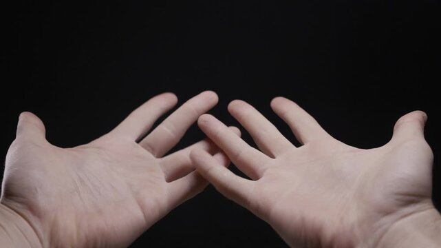 Man's hands moving and fidgeting expressively against a plain black background. Concept of anxiety, stress, non-verbal communication, overthinking, creativity, and inner turmoil