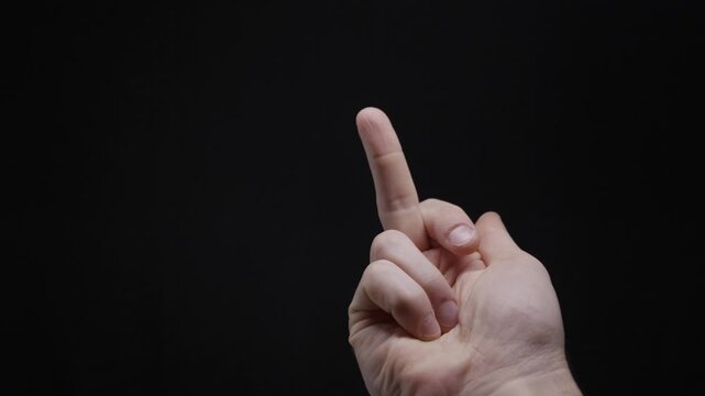 Male hand displays the middle finger in an offensive gesture against a dark black background. This concept represents rudeness, anger, denial, and defiant social behavior.